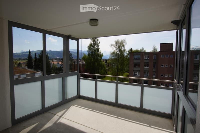 Spacious balcony with large windows offering a scenic mountain view, modern railing, and clean tiled floor.