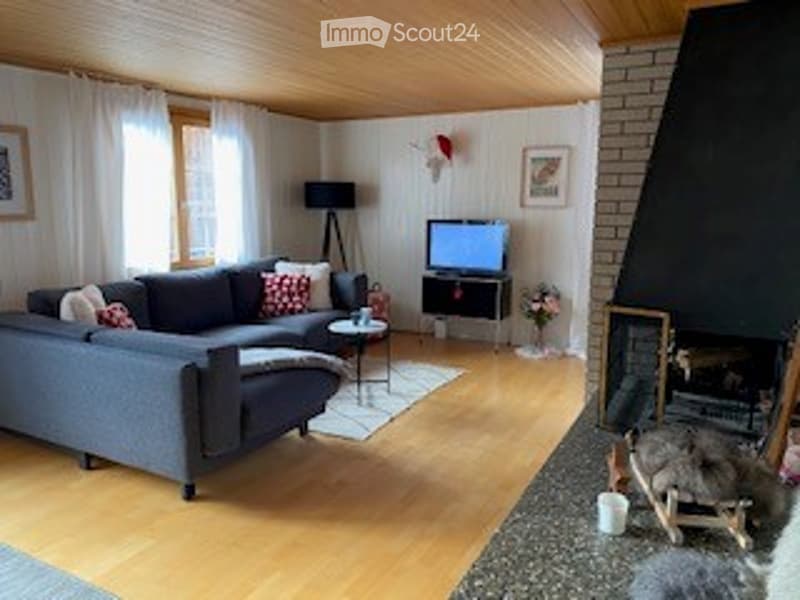 Bright living room with wooden ceiling and floors, grey sectional sofa, coffee table, TV, fireplace, and decorative items.