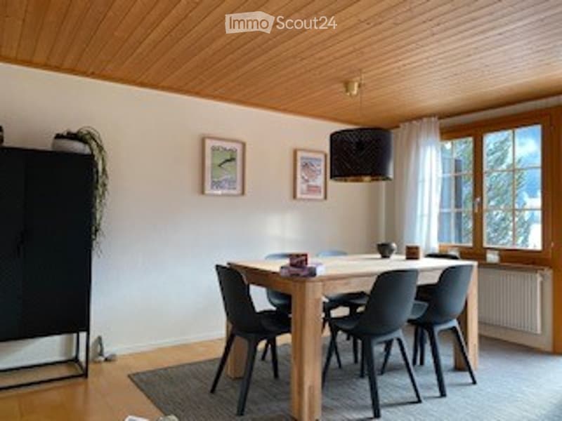 Bright dining room with wooden ceiling, white walls, large window, dining table with chairs, cabinet, and picture frames on the wall.