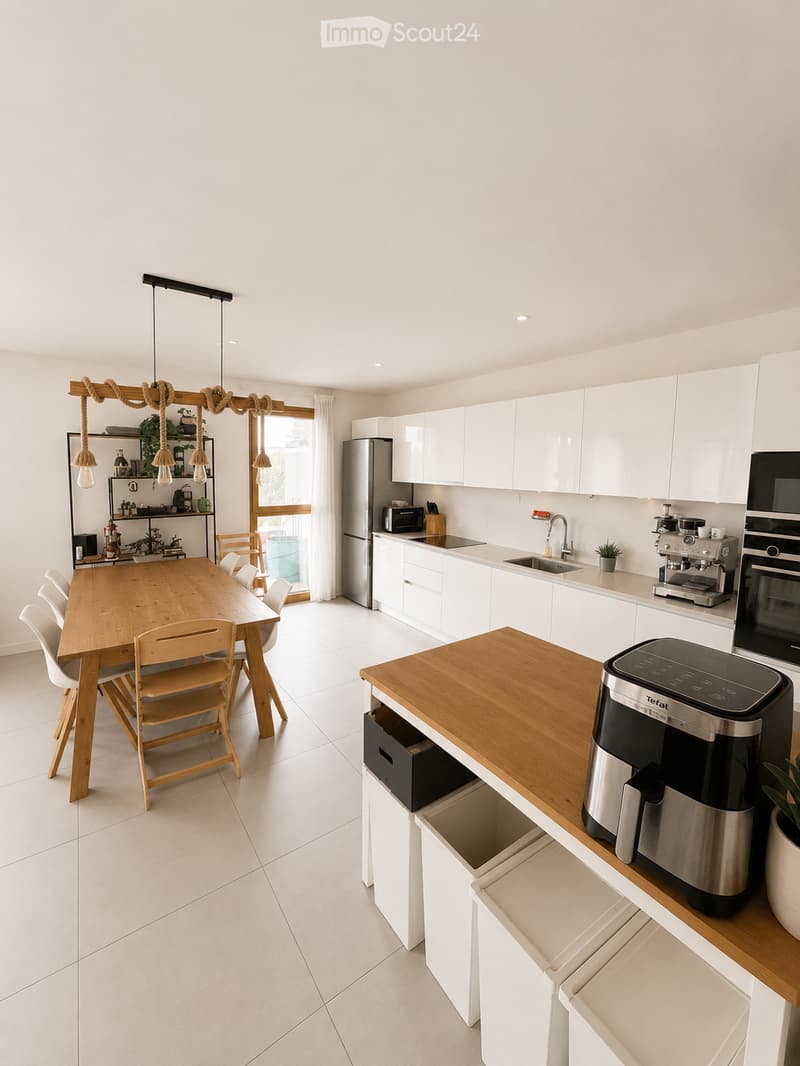 Modern kitchen with white cabinets, wooden dining table, six chairs, stainless steel appliances, and pendant lighting.