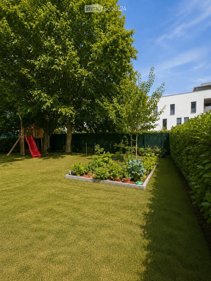 Well-maintained garden with a lawn, raised vegetable bed, small play structure with a slide, and surrounding trees and shrubs.
