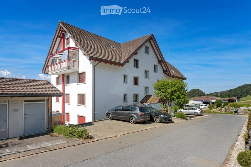 Two-story house with white walls, red trim, tiled roof, balcony, garage, and several parked cars.