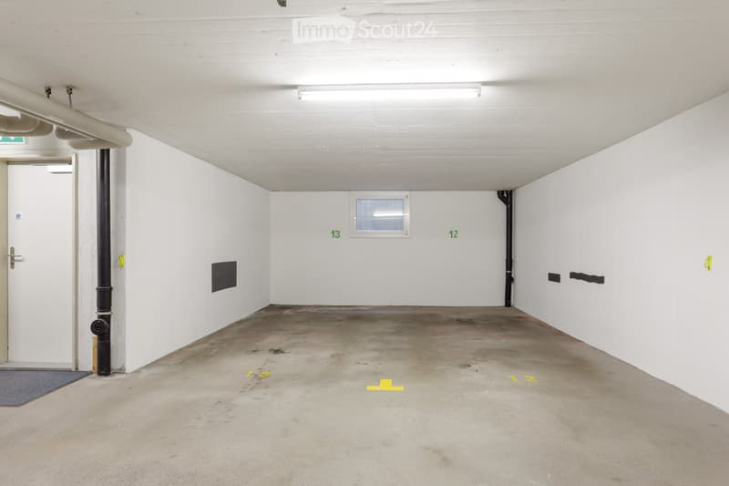 Empty underground parking space with white walls, concrete floor, and numbered parking spots marked on the floor.