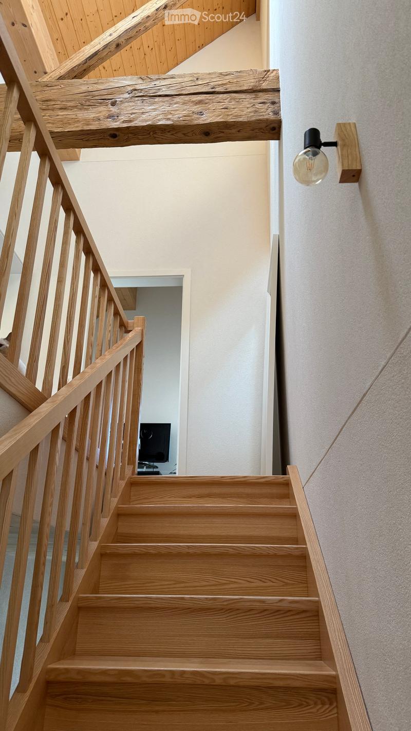 Wooden staircase with a handrail and a wall-mounted light fixture, leading to an open doorway.