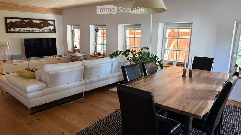 A modern living room with a white leather sofa, wooden dining table, black chairs, television, and decorative items.