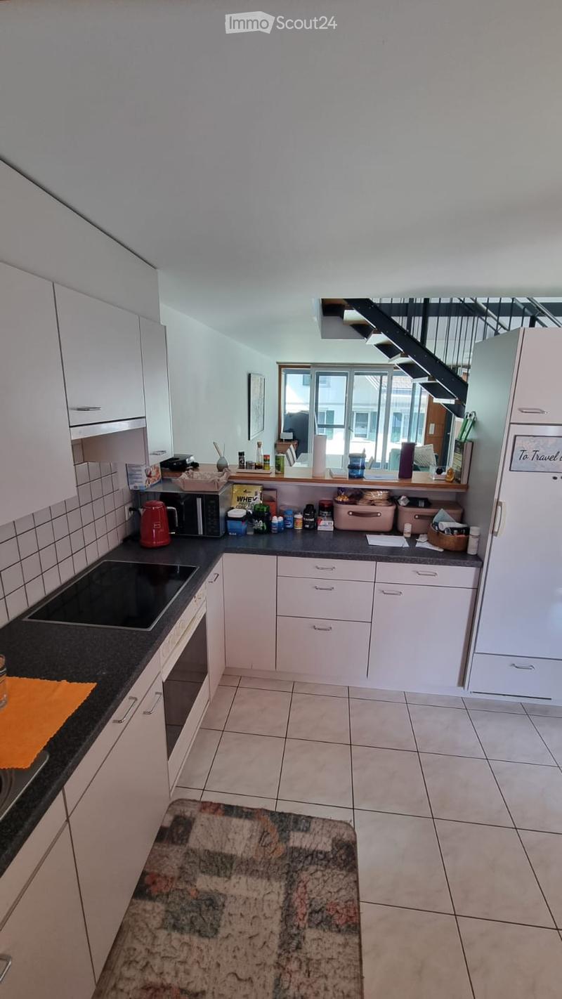 Modern kitchen with white cabinets, black countertops, and various appliances including a microwave, oven, and refrigerator. The space features a tiled floor and a small dining area with a marble table.