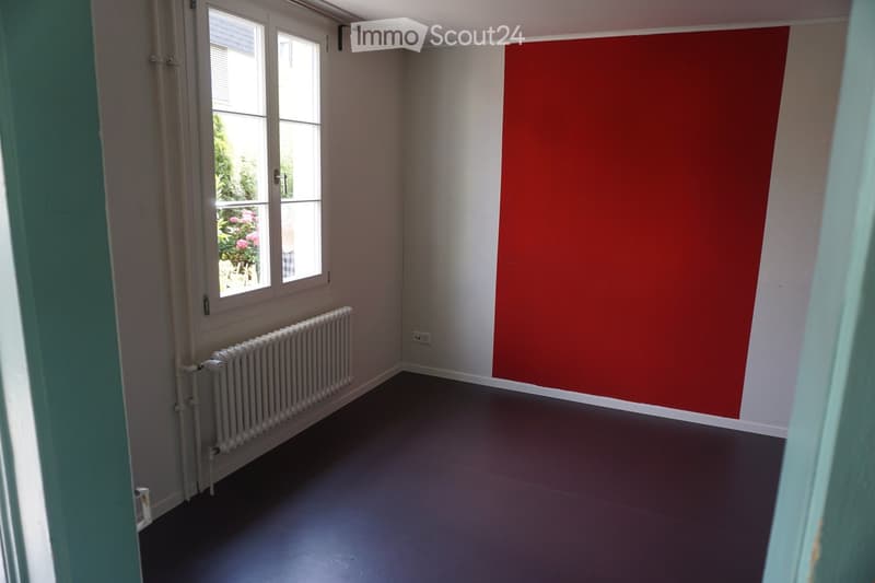 Empty room with grey walls, dark flooring, a single window with white frame, and a white radiator below the window.