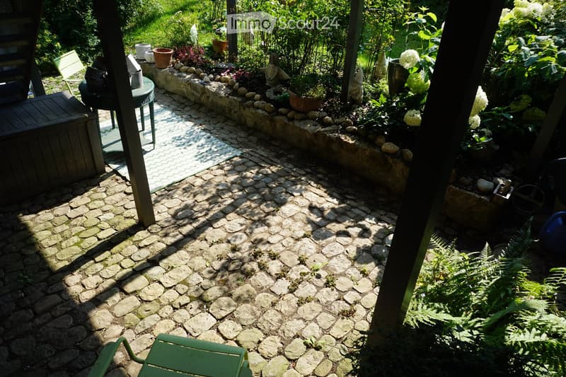 A well-maintained garden with a stone-paved pathway, surrounded by lush greenery, potted plants, and decorative elements.