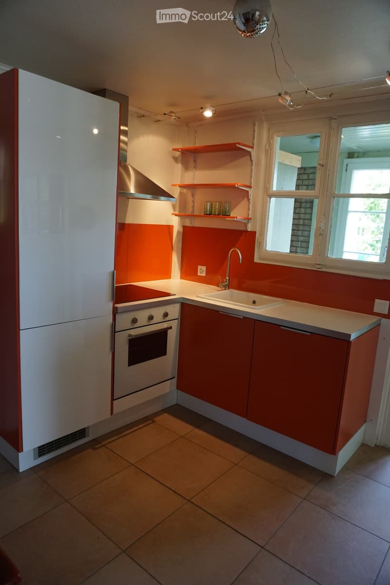 Modern kitchen with white and red cabinets, stainless steel appliances, and a central island with a sink and faucet. The walls are painted in a bright orange color, and the floor is tiled.