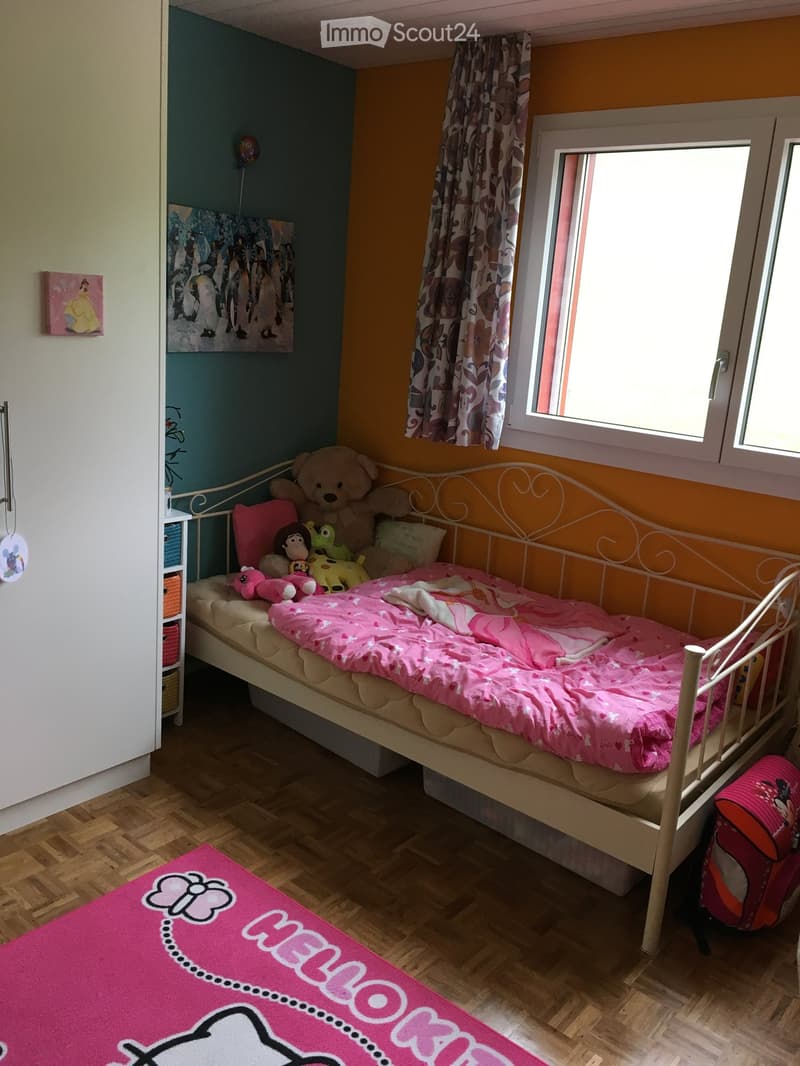 Single bed with mattress, stuffed toys, pink blanket, rug, yellow walls, wardrobe, two-pane window with curtain, small shelf with baskets