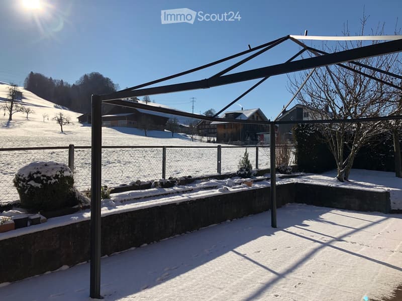 covered terrace, metal frame, snowy landscape in the background, chain-link fence, bushes