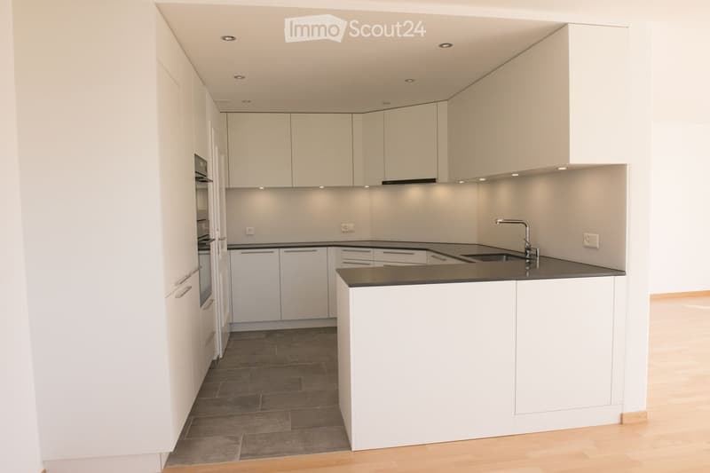 Modern kitchen with white cabinets, dark countertops, and a central island. Features include a sink with a modern faucet, built-in oven, and recessed ceiling lighting.