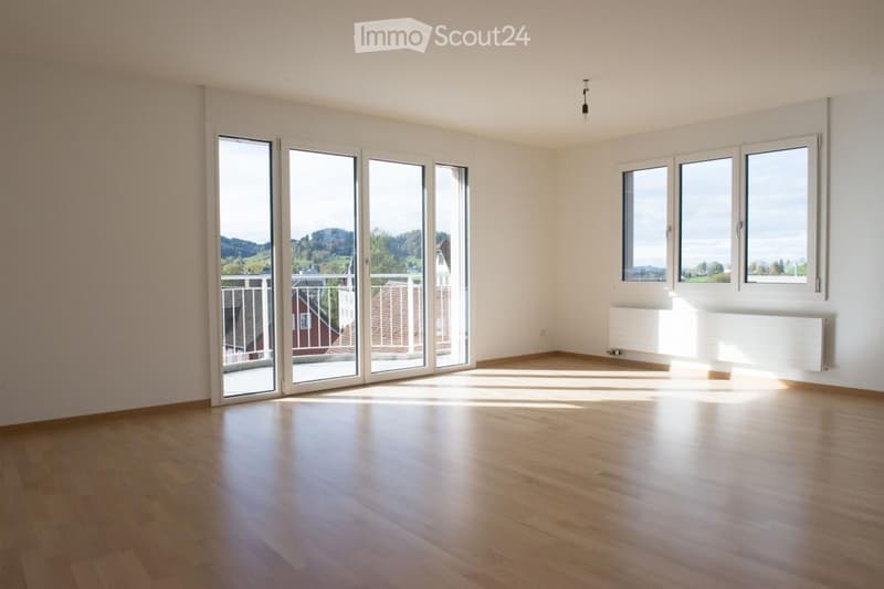 Empty room with wooden flooring, large windows, and sliding glass doors leading to a balcony.