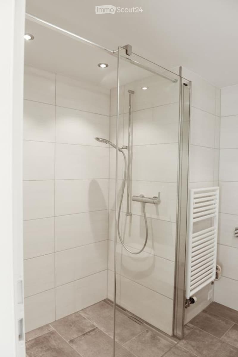 Modern bathroom with a glass-enclosed shower, white tiles, and a towel rack.