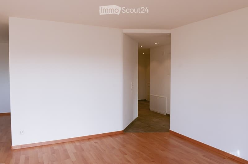 Empty room with wooden flooring and white walls, featuring a doorway leading to another room with a radiator visible.