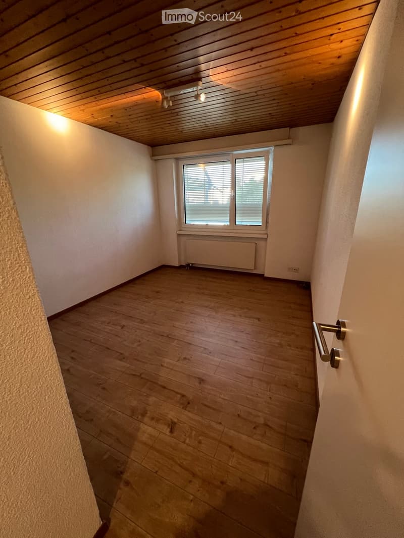 Empty room with wooden floor, white walls, and a window with blinds. The ceiling is wooden with recessed lighting.
