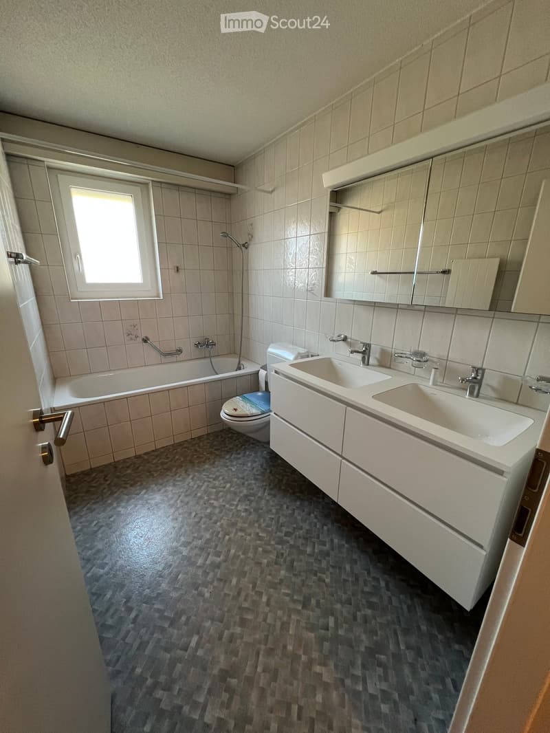 Bathroom with a bathtub, toilet, double sink, mirror, and tiled walls and floor.