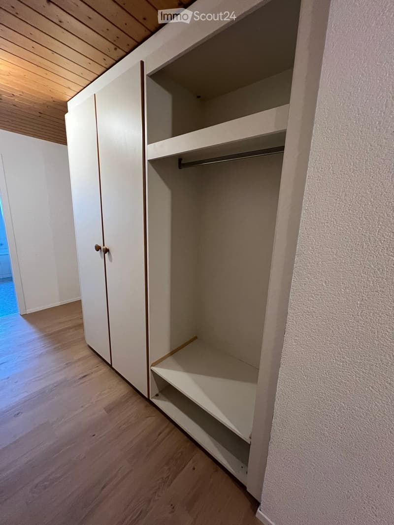 Empty closet with white sliding doors, wooden floor, and built-in shelves and hanging rod.