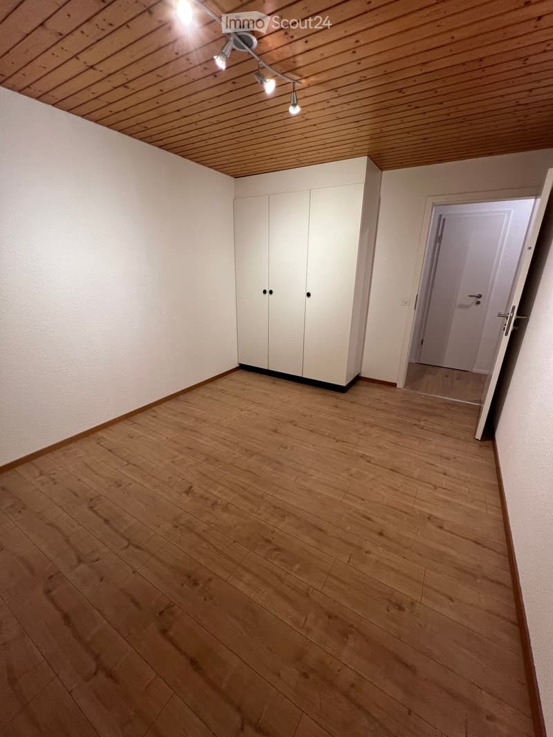 Empty room with wooden flooring, white walls, built-in white closet, and a doorway leading to another space.