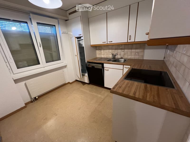 Modern kitchen with white cabinets, wooden countertops, a sink, and a dishwasher. The space features a large window with blinds and a tiled backsplash.