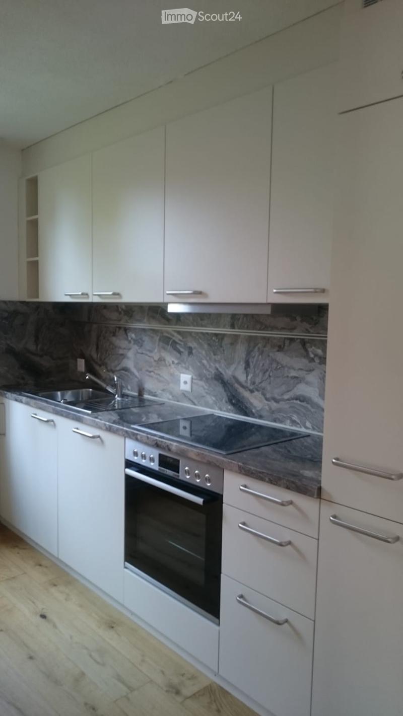 Modern kitchen with white cabinets, marble backsplash, stainless steel sink, and built-in oven.