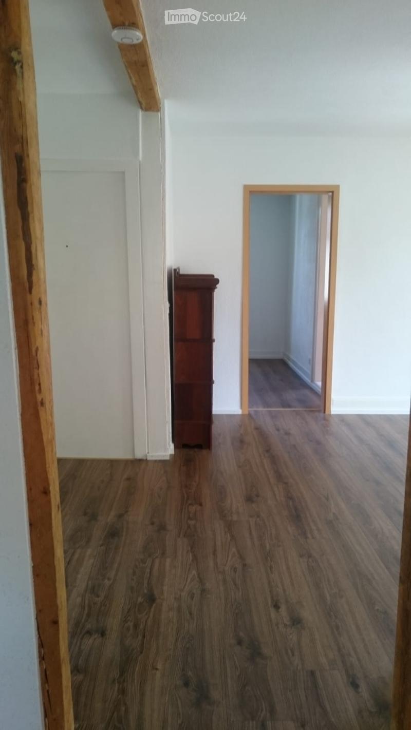 A small, unfurnished hallway with wooden flooring and white walls. A single wooden cabinet is positioned against the wall, and a doorway leads to another room.