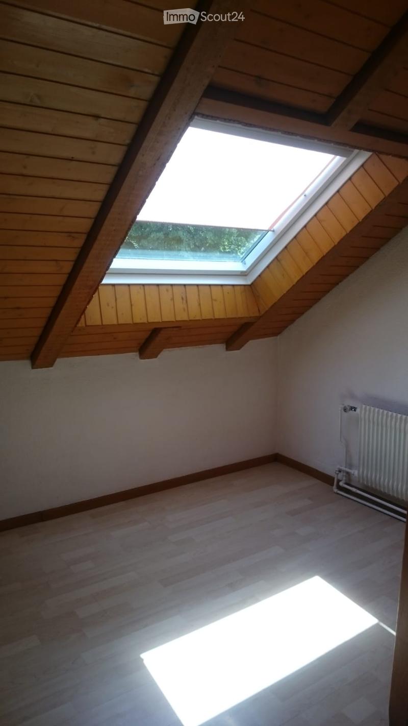Empty attic room with wooden ceiling, skylight window, wooden floor, and radiator on the wall.