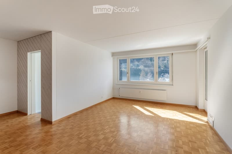 Empty room with wooden flooring, white walls, large windows, and a radiator. No furniture or equipment present.