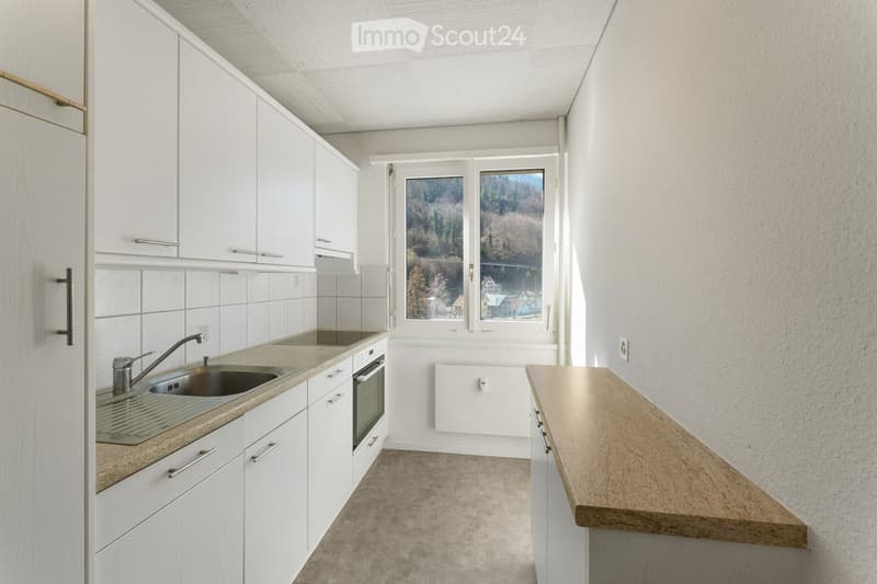 Modern kitchen with white cabinets, stainless steel sink, and a wooden countertop. The space features a view of a forested area through large windows.