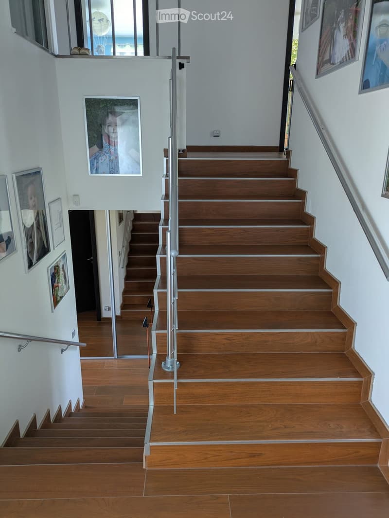 Wooden staircase with metal handrails, white walls, and framed pictures on the walls.