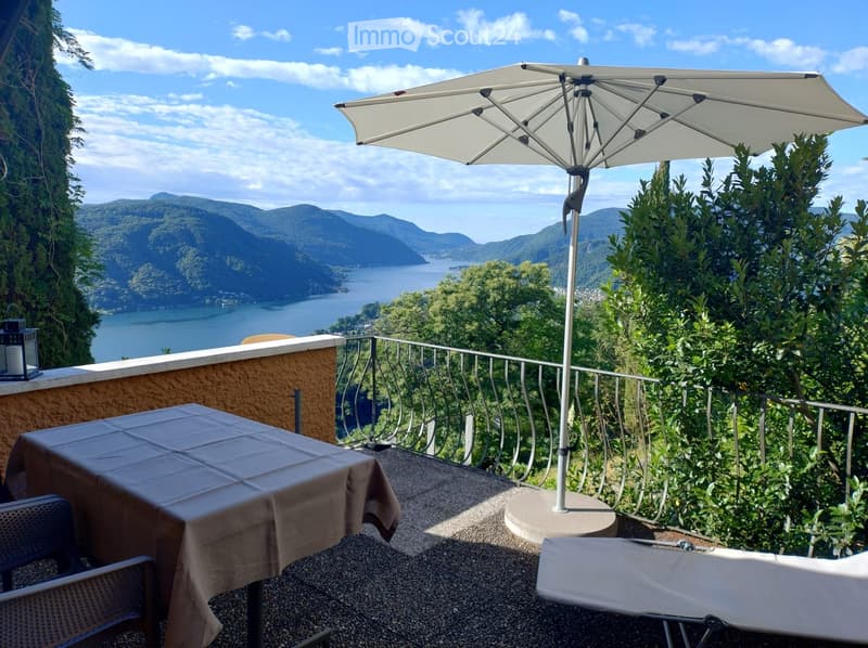 Balcony with a scenic lake view, featuring a table, chairs, umbrella, and lounge chair.