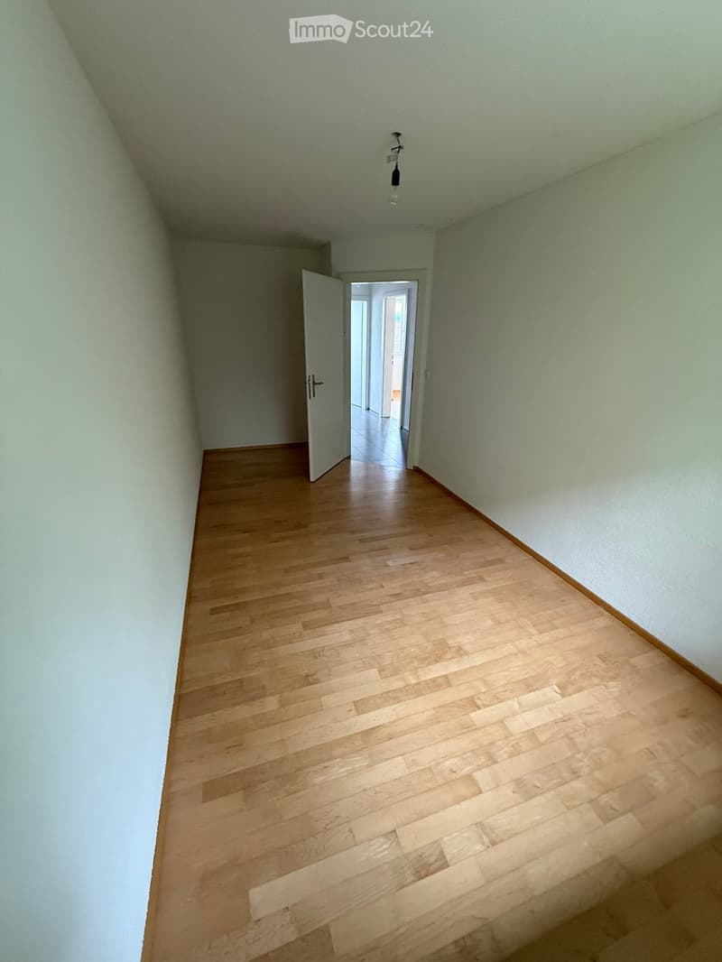 Empty hallway with wooden flooring, white walls, and a single open door leading to another room.