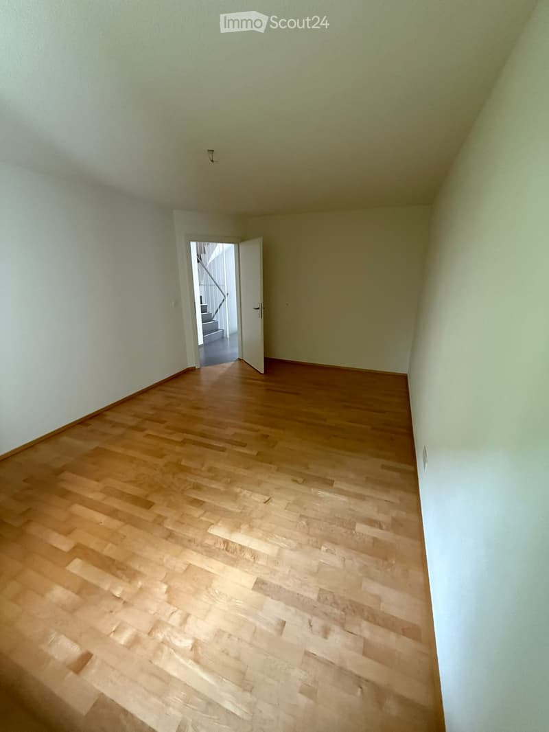 Empty room with light-colored wooden flooring and white walls, featuring an open doorway leading to a staircase.