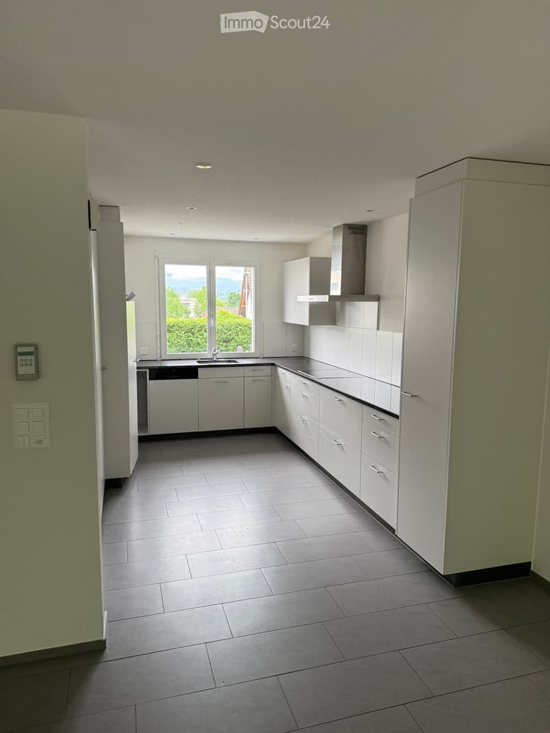 Empty kitchen with white cabinets, stainless steel appliances, tiled floor, and large windows overlooking greenery.