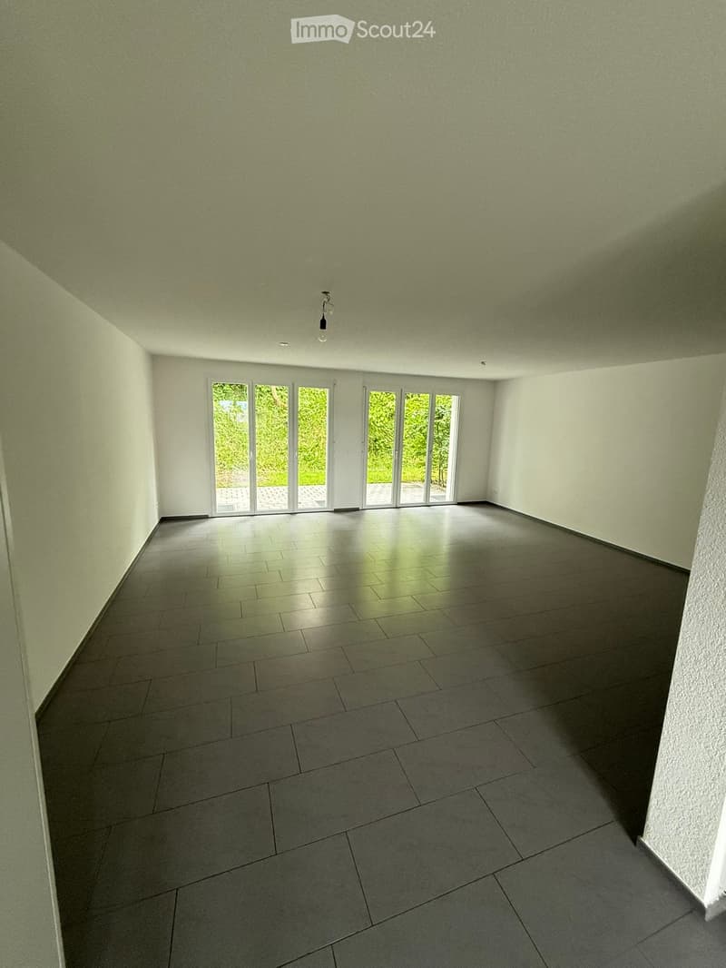 Empty room with light green walls, grey tiled floor, and large glass doors leading to an outdoor area.