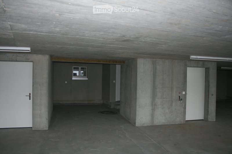 Empty basement room with concrete walls, two white doors, a small window, and a round hatch in the floor.