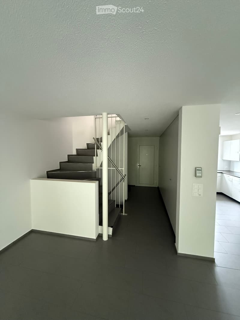 Modern hallway with dark tiled floor, white walls, staircase with metal railing, and a door leading to another room.