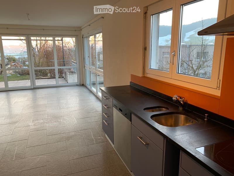 Modern kitchen with dark countertops, stainless steel sink, grey cabinets, and large windows overlooking a garden area.