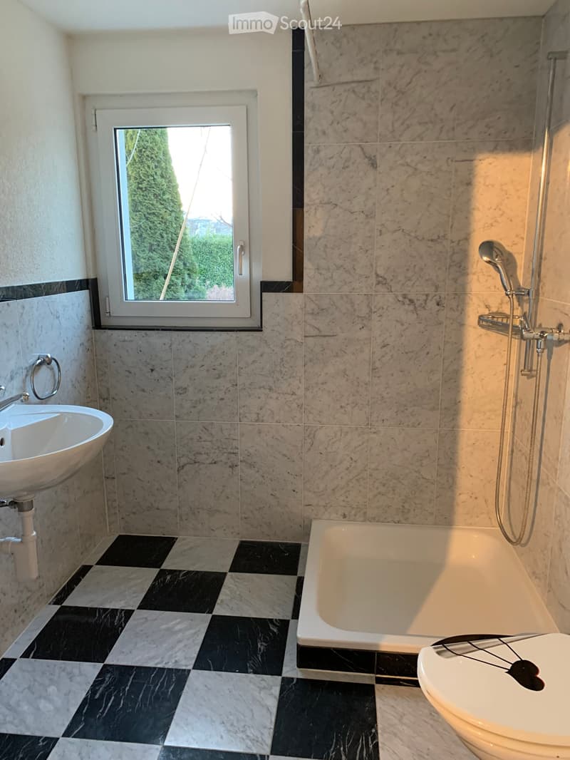 Modern bathroom with marble tiles, black and white checkered floor, bathtub, toilet, sink, and showerhead.