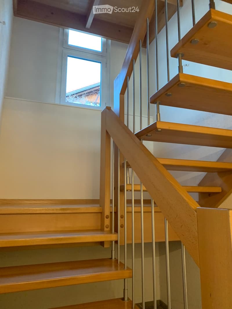Wooden staircase with metal balustrade, light-colored walls, and a small window at the top.