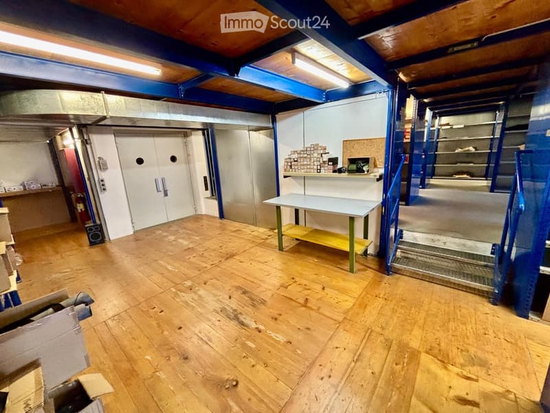 Empty room with wooden flooring, exposed ceiling beams, and a few storage items and shelves in the background.