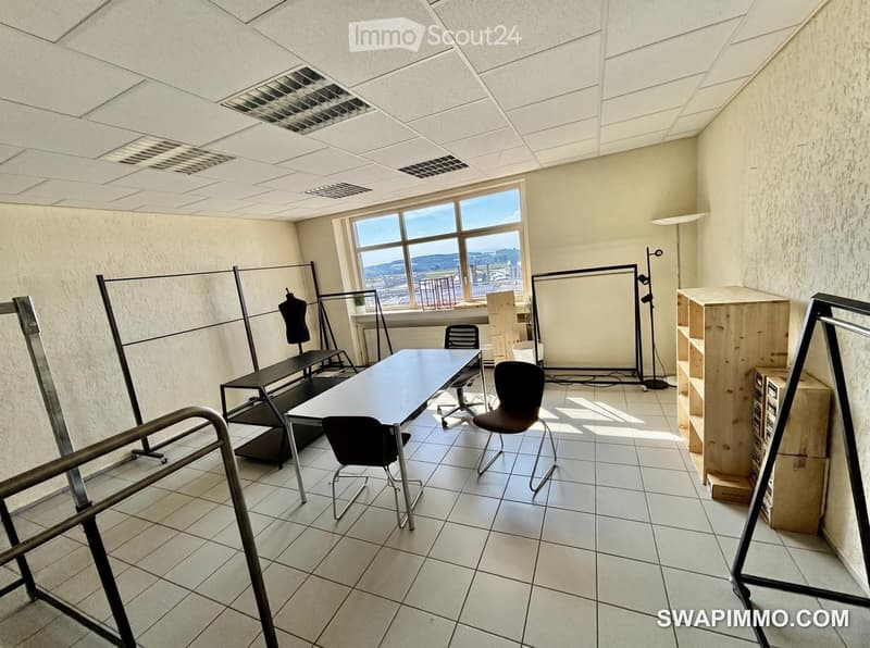 Office space with a large window, tiled floor, and minimal furniture including a table, chairs, a shelf, and a mannequin.