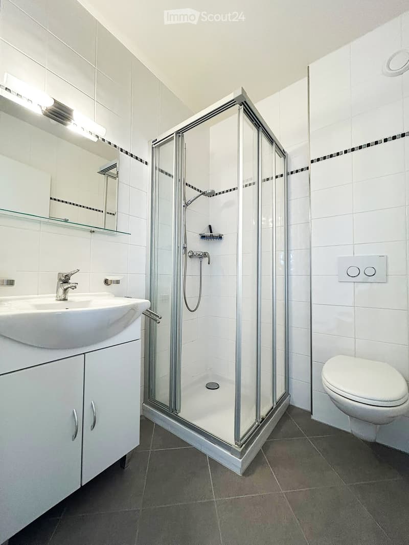 Modern bathroom with white tiles, a glass-enclosed shower, a white sink with a chrome faucet, a mirrored cabinet, and a toilet.
