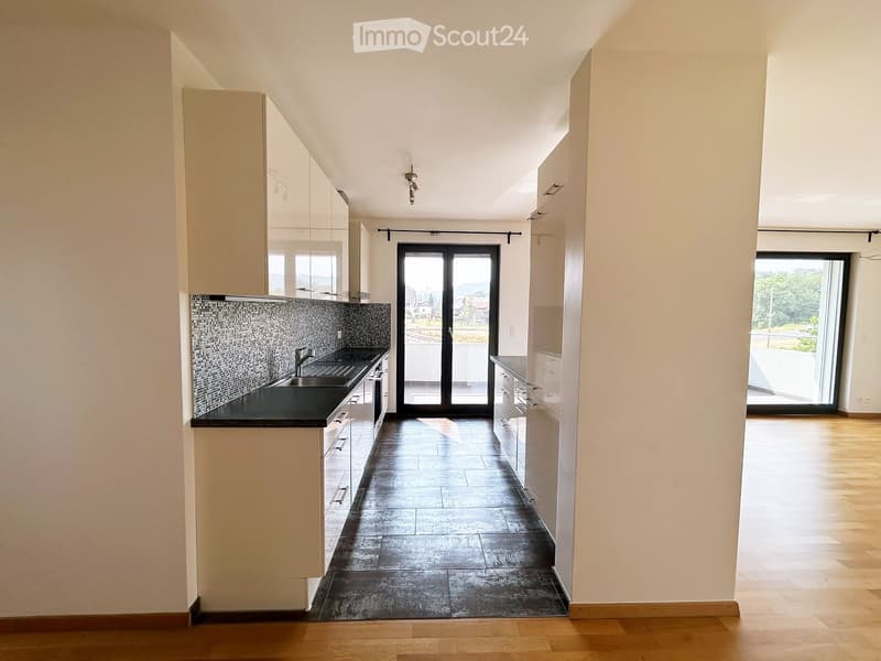 Modern kitchen with white cabinets, black countertop, and dark tiled floor. Features a sink, faucet, and large sliding glass doors leading to a balcony.