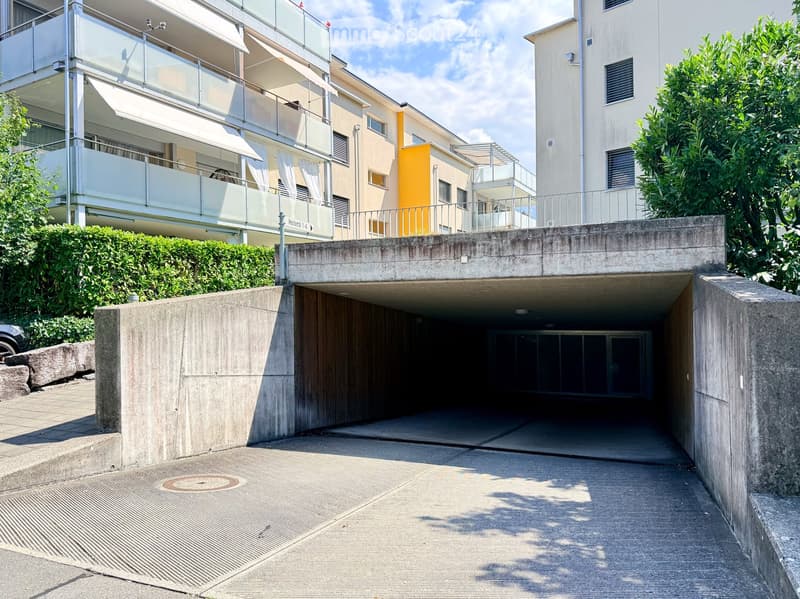 Modern multi-story residential building with balconies, glass railings, and a covered underground parking area.