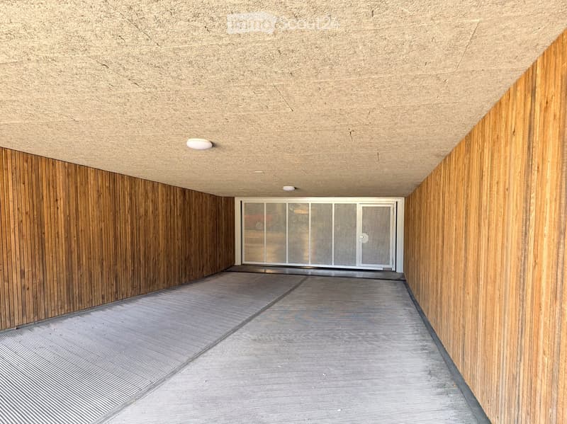 A modern corridor with wooden panel walls, a textured concrete ceiling, and a glass door at the end.