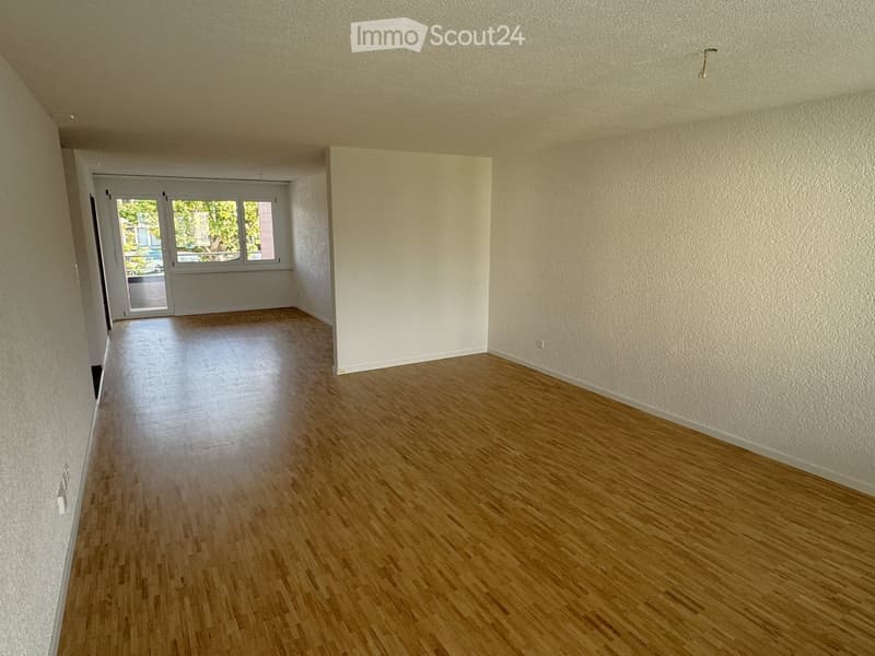 Empty room with hardwood floors, white walls, double doors leading to a balcony with a glass wall.