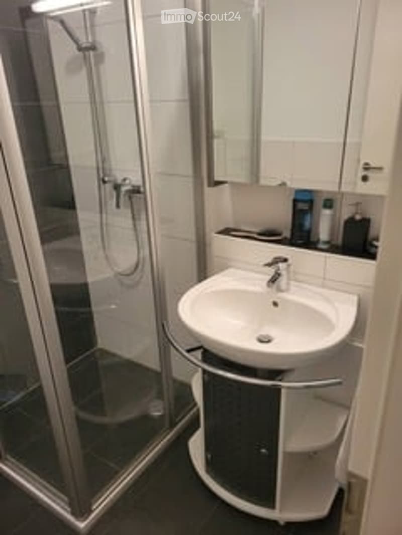 Modern bathroom with a white sink, mirrored cabinet, and glass-enclosed shower. The space features clean lines and a sleek design.