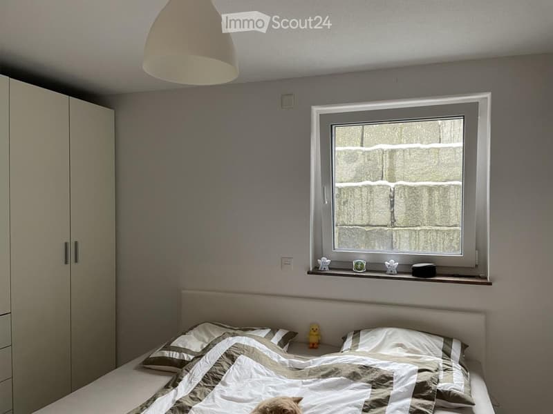 A cozy bedroom with a bed, pillows, a blanket, a wardrobe, a window with frosted glass, and decorative items on the windowsill.