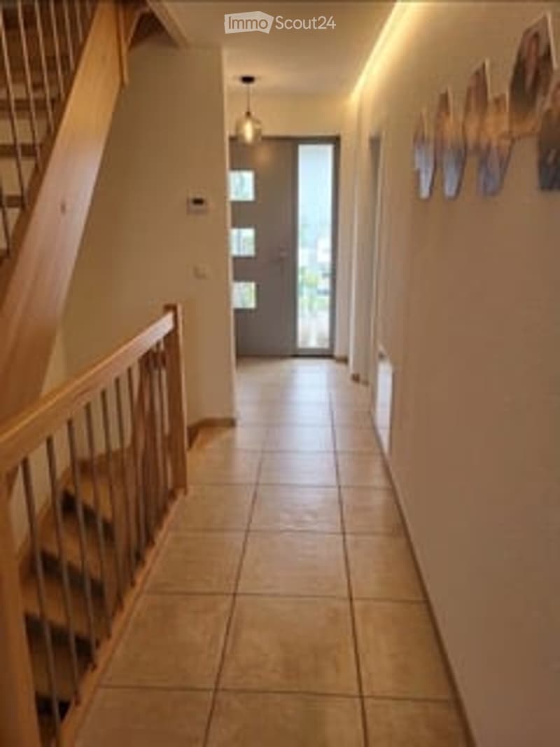 Hallway with tiled floor, wooden staircase railing, and modern lighting fixtures.